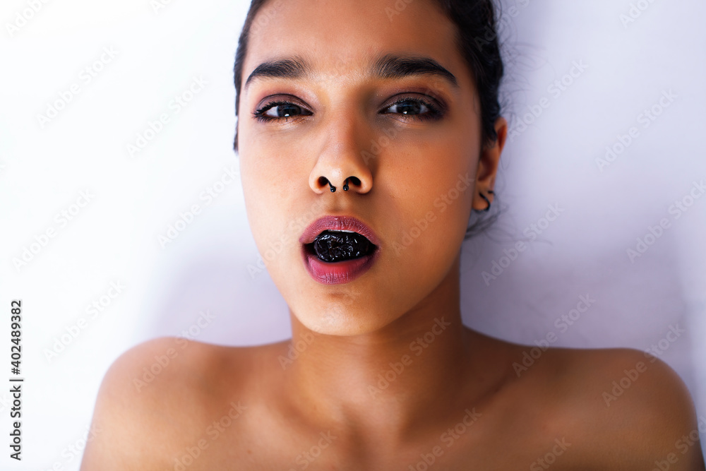 young pretty indian woman with dry fruit in mouth on white background young pretty indian woman with dry fruit in mouth on white background
