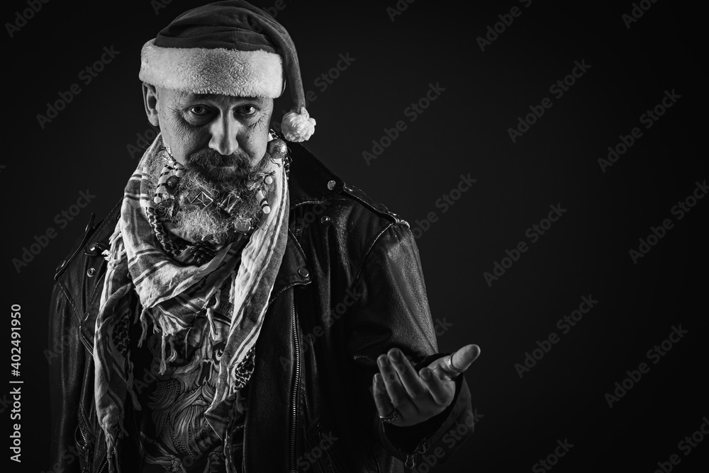 a young, handsome, serious man with a long beard on which hang Christmas toys, a man in a black jacket and a Christmas hat on his head on a dark background, emotional. There is a place for an inscript