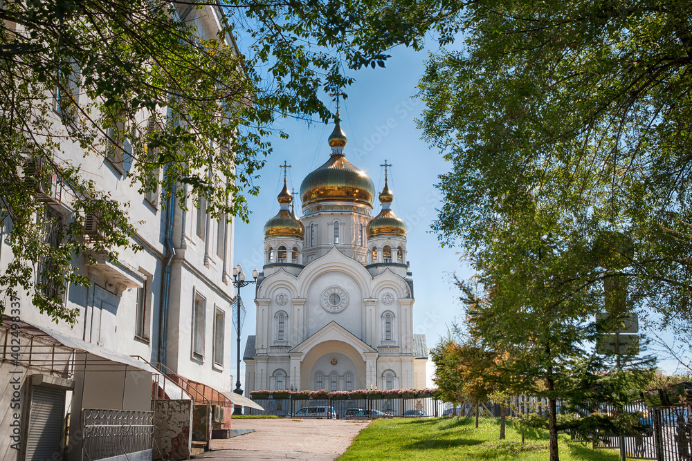 A traditional Russian church with golden domes against a blue sky and a green branch frame.