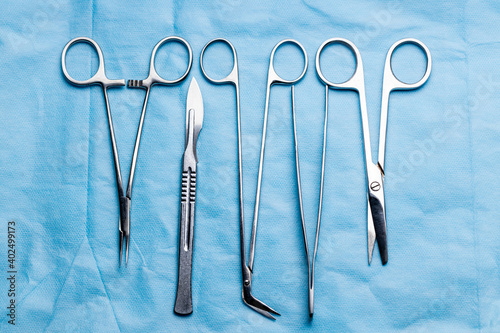 stack of surgical equipment at surgery desk. medical tools such scissors, scalpel, forceps, tweezers over blue background. surgery concept