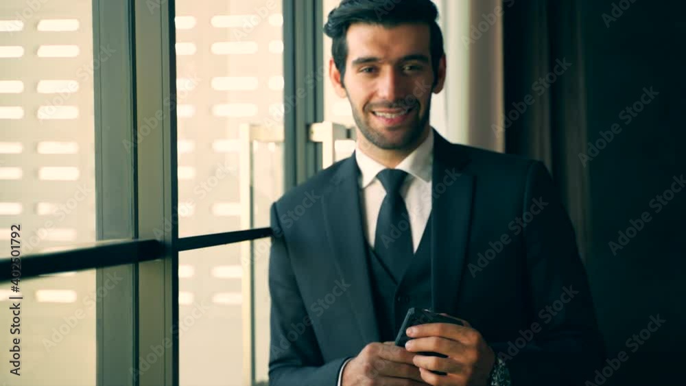 Young businessman standing at the mirror in the office. Successful young business man looks Downtown office window. Medium close up with sunrise sky and some sunlight flare. Young businessman standing at the mirror in the office. Successful young business man looks Downtown office window. Medium close up with sunrise sky and some sunlight flare.
