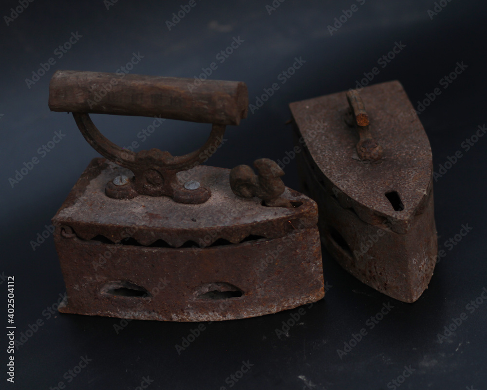 Old rusty antique iron for ironing clothes with the help of charcoal. Household antiques. Iron for clothes made of traditional steel with a wooden handle (Ayam Jago). Detailed photo of an old iron. Old rusty antique iron for ironing clothes with the help of charcoal. Household antiques. Iron for clothes made of traditional steel with a wooden handle (Ayam Jago). Detailed photo of an old iron.