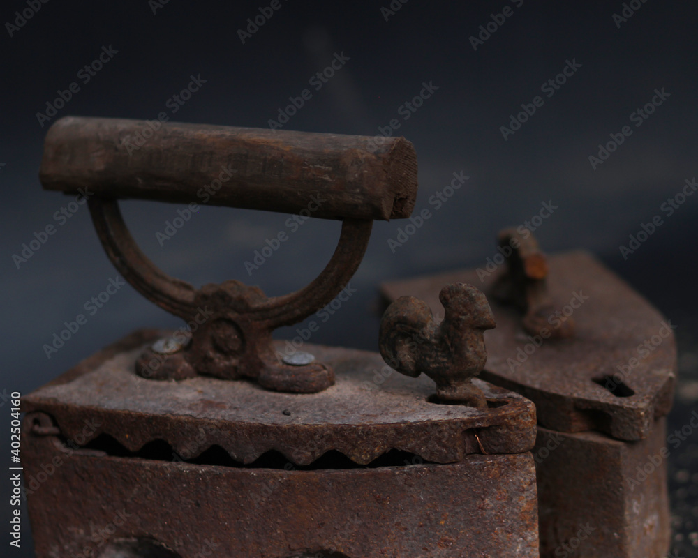 Old rusty antique iron for ironing clothes with the help of charcoal. Household antiques. Iron for clothes made of traditional steel with a wooden handle (Ayam Jago). Detailed photo of an old iron. Old rusty antique iron for ironing clothes with the help of charcoal. Household antiques. Iron for clothes made of traditional steel with a wooden handle (Ayam Jago). Detailed photo of an old iron.