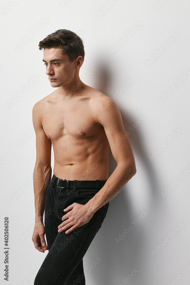 A guy in black trousers stands against a wall in a cropped view A guy in black trousers stands against a wall in a cropped view