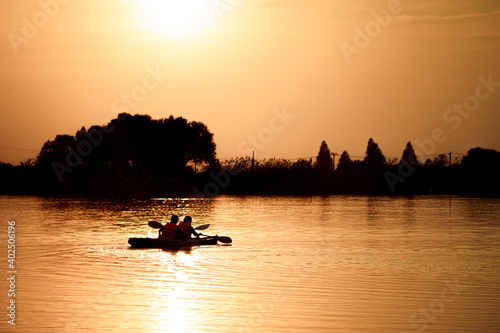 Silhouette of active fluent kayak of female couples, leisure travel tourism, adventure style in a calm atmosphere in the lake, is a fun excursion of a boat in the golden light in the evening.