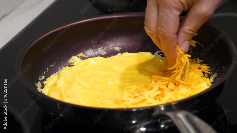 Adding Grated Cheddar Cheese to Egg Omelet in Frying Pan - Kitchen Cooking Adding Grated Cheddar Cheese to Egg Omelet in Frying Pan - Kitchen Cooking