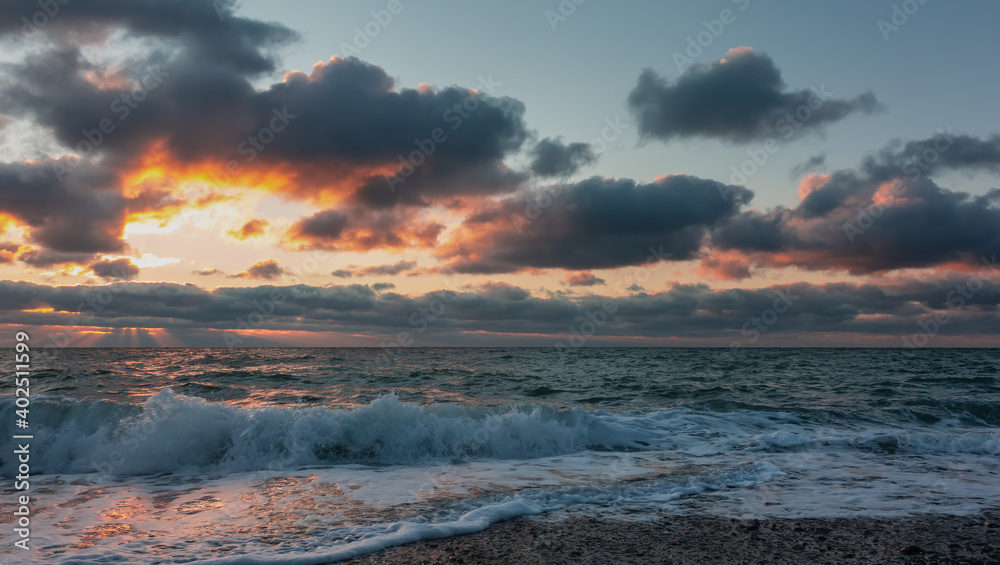 Seascape at sunset. The sun's rays make their way through the clouds, illuminating the sky in shades of pink and gold. Sunny path on the water. Waves roll ashore with foam and spray. Black Sea Seascape at sunset. The sun's rays make their way through the clouds, illuminating the sky in shades of pink and gold. Sunny path on the water. Waves roll ashore with foam and spray. Black Sea