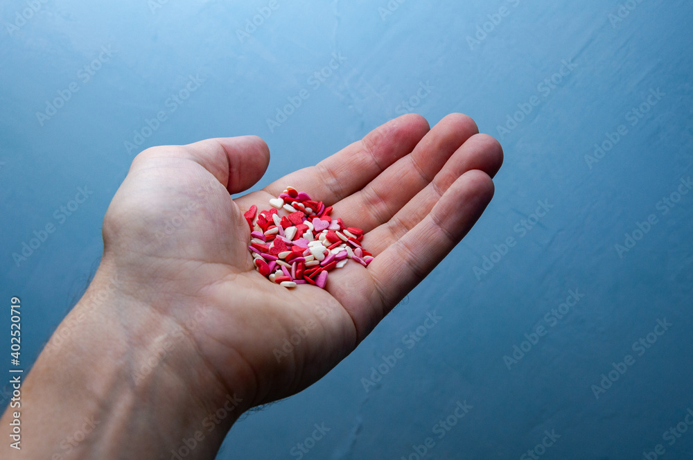 A hand holds a handful of hearts. Charity. Valentine's Day concept on a blue background. A hand holds a handful of hearts. Charity. Valentine's Day concept on a blue background.