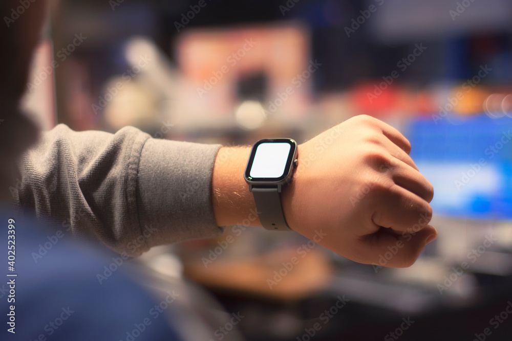 A man with a smartwatch and a white screen mockup on his hand. A man uses a fitness tracker on the background of a shopping mall. A man with a smartwatch and a white screen mockup on his hand. A man uses a fitness tracker on the background of a shopping mall.