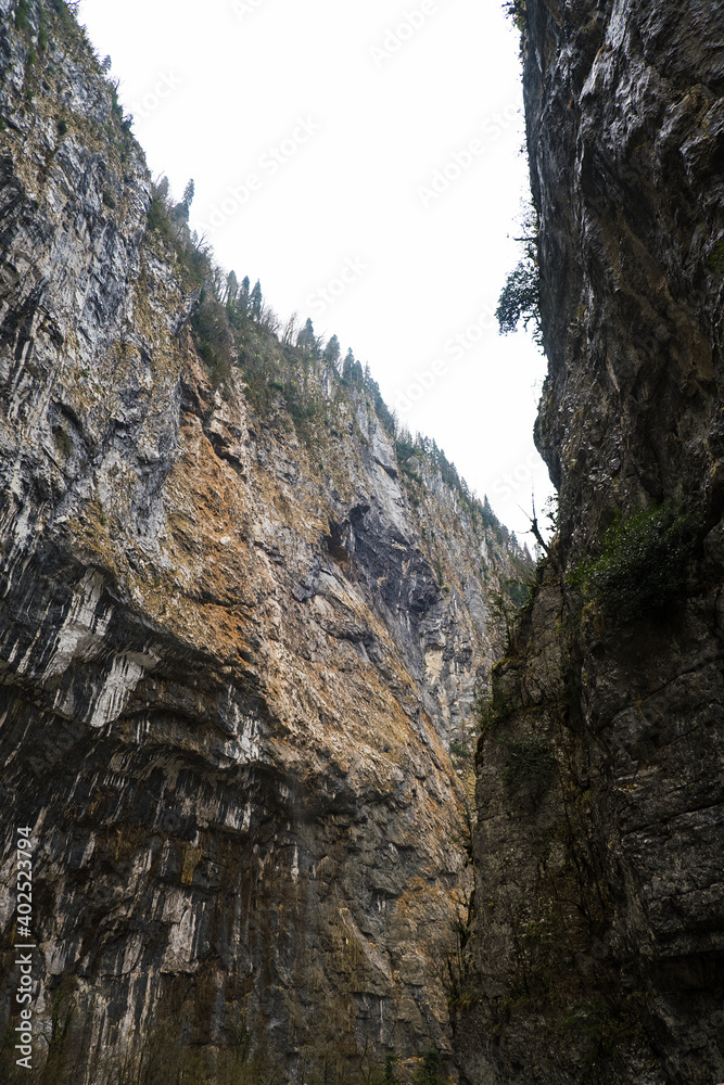 View from below of a mountain gorge with high cliffs and clouds, cloudy autumn day