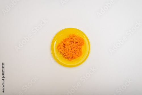 An ingredient for making various salads and snacks. Mashed boiled carrots in a yellow plate isolated on a white background. Flat lay