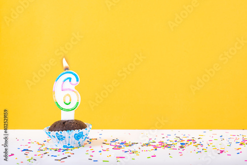 6 number candle on a cup cake with colorful sprinkles and yellow background sixth birthday anniversary celebrations