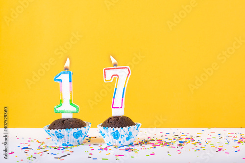 17 number candle on a cup cake with colorful sprinkles and yellow background seventeenth birthday anniversary celebrations