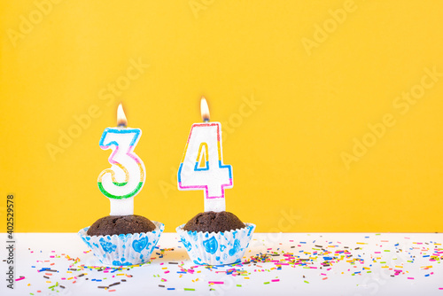 34 number candle on a cup cake with colorful sprinkles and yellow background thirty fourth birthday anniversary celebrations photo
