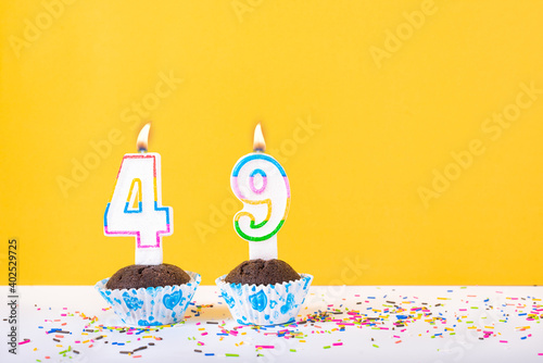 49 number candle on a cup cake with colorful sprinkles and yellow background forty ninth birthday anniversary celebrations. photo
