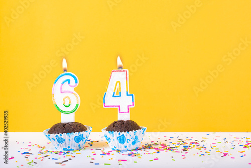 64 number candle on a cup cake with colorful sprinkles and yellow background sixty fourth birthday anniversary celebrations photo