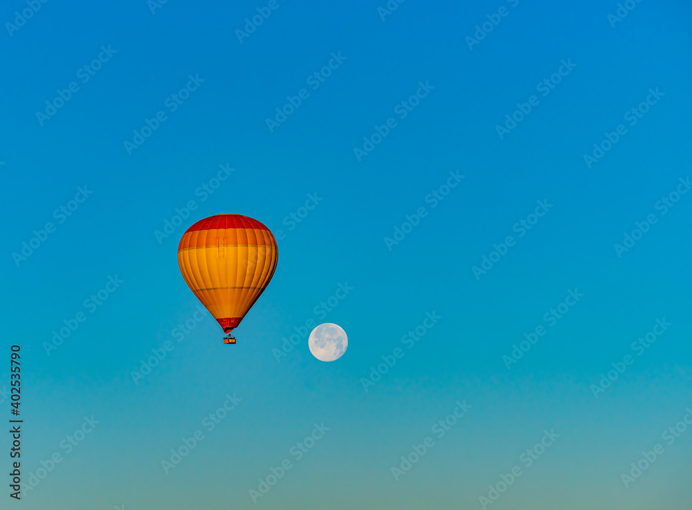 Obraz premium Hot air balloon flying over Cappadocia with full moon, in blue sky