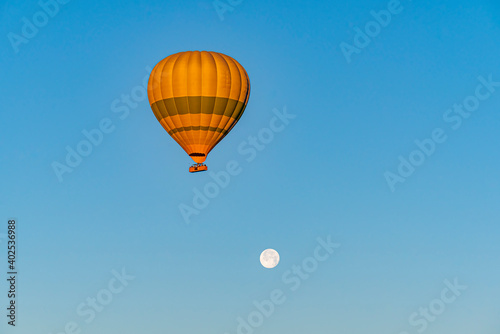 Hot air balloon flying over Cappadocia with full moon, in blue sky
