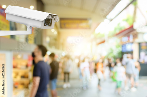 Modern public CCTV camera with blur crowd and shopping plaza background. Recording cameras for monitoring all day and night. Concept of surveillance and monitoring with copy space.