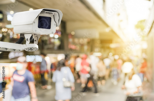 Modern public CCTV camera with blur crowd and shopping plaza background. Recording cameras for monitoring all day and night. Concept of surveillance and monitoring with copy space.
