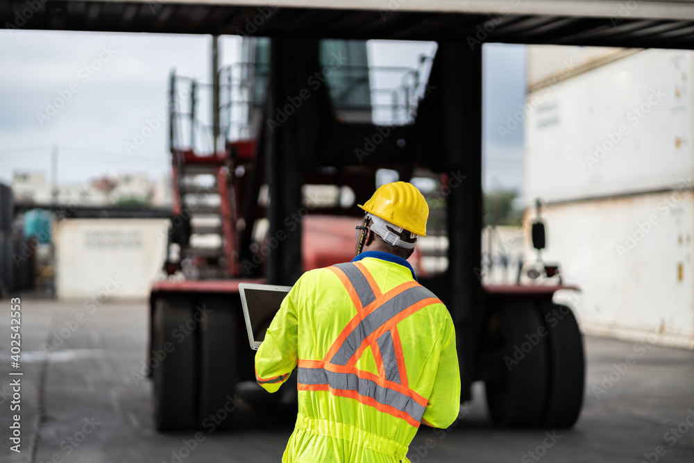 African technician dock worker in protective safety jumpsuit uniform and with hardhat and use digital tablet at cargo container shipping warehouse. transportation import,export logistic industrial African technician dock worker in protective safety jumpsuit uniform and with hardhat and use digital tablet at cargo container shipping warehouse. transportation import,export logistic industrial