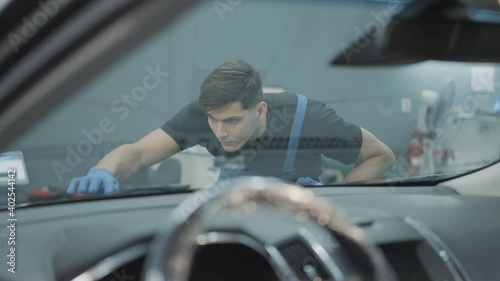 Shooting from car salon of concentrated handsome service man examining tuning of hood. Portrait of Caucasian professional brunette employee checking work in repair shop.