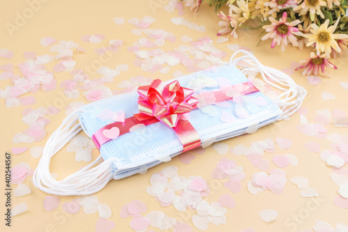 Medical protective masks with pink bow, flower and confetti isolated on pastel background. Flat lay. Gift for holiday, birthday, Mother's Day, Valentine's day, Women's Day during coronavirus pandemic.