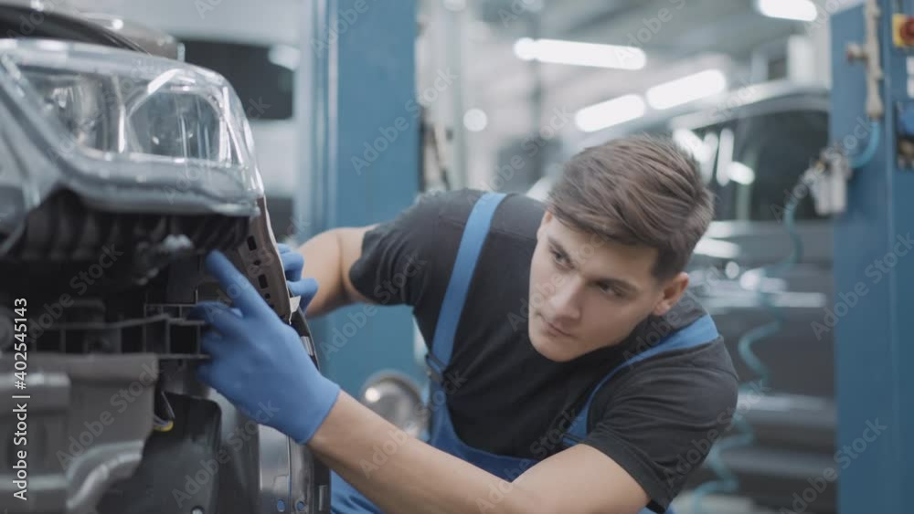 Portrait of handsome auto mechanic checking breakage of disassembled car in repair shop. Concentrated young Caucasian service man examining auto parts indoors. Portrait of handsome auto mechanic checking breakage of disassembled car in repair shop. Concentrated young Caucasian service man examining auto parts indoors.