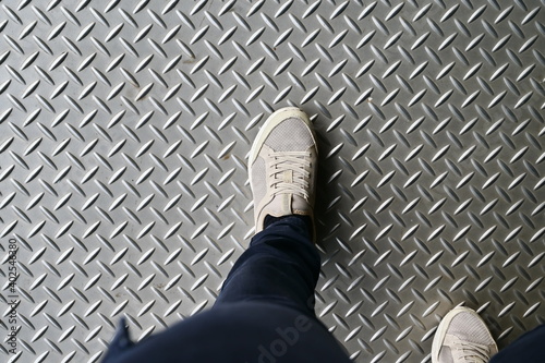 A woman in a sneakers stands on a walkway on a bus, passenger boat, or overpass (Metal chicken paw pattern painted in dark gray for areas with slippage).
