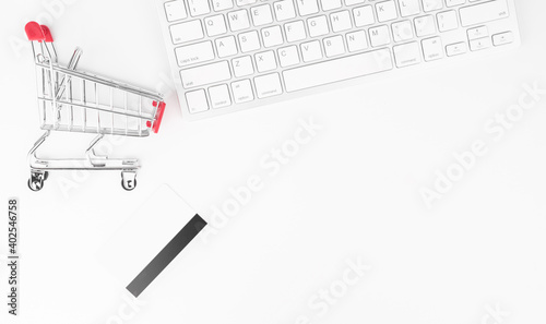 Online shopping concept. Small red trolley,keyboard and credit card on the table.