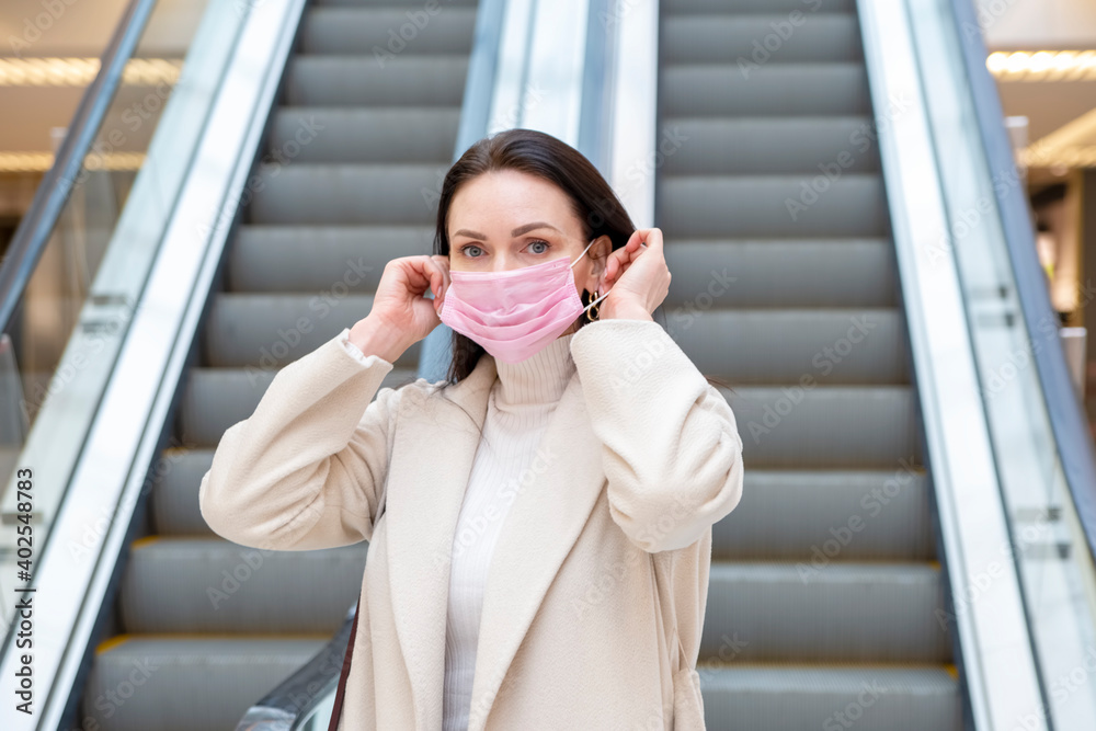 Fototapeta premium beautiful woman putting on pink medical mask on her face against the background of the escadator in a public place