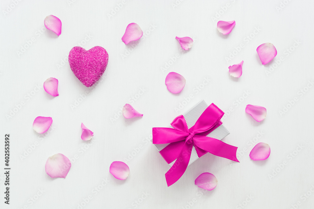 Valentine's day, festive composition. Purple heart, purple rose petals and a gift box with purple ribbon. White wooden background. Top view, flat lay.