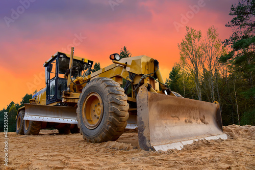 Motor Grader on road construction in forest area. Greyder leveling the sand, ground and gravel during road work. Heavy machinery and construction equipment for grading. Earthworks grader machine photo