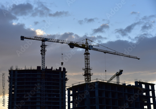 Silhouettes of tower cranes on awesome sunset background. Preparing to pour a bucket of concrete into formwork. Construction a multi-storey residential building. Small sharpness, possible granularity