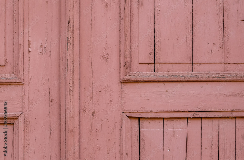 Fragment of an old wooden door painted with pink paint. A background from an old surface with cracked paint. Selective focus. Fragment of an old wooden door painted with pink paint. A background from an old surface with cracked paint. Selective focus.