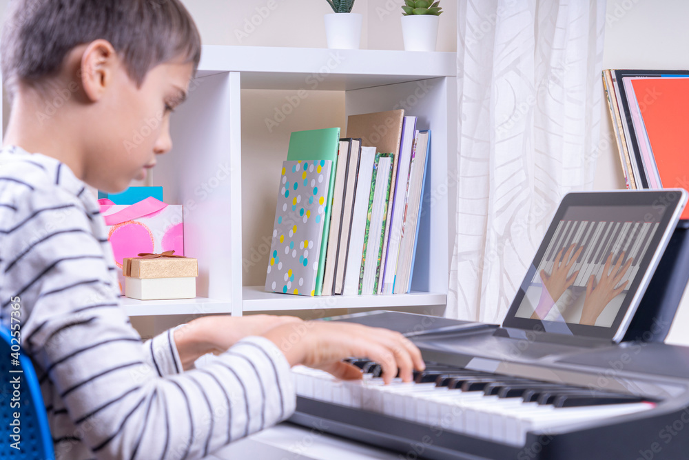 Boy watching video lesson at digital tablet computer and playing piano at home. Online learning remote education Boy watching video lesson at digital tablet computer and playing piano at home. Online learning remote education