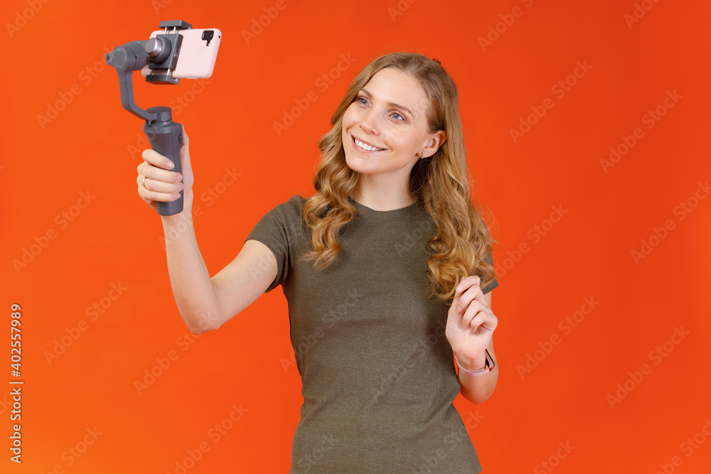 Portrait of attractive young girl taking selfie on smartphone isolated on orange background