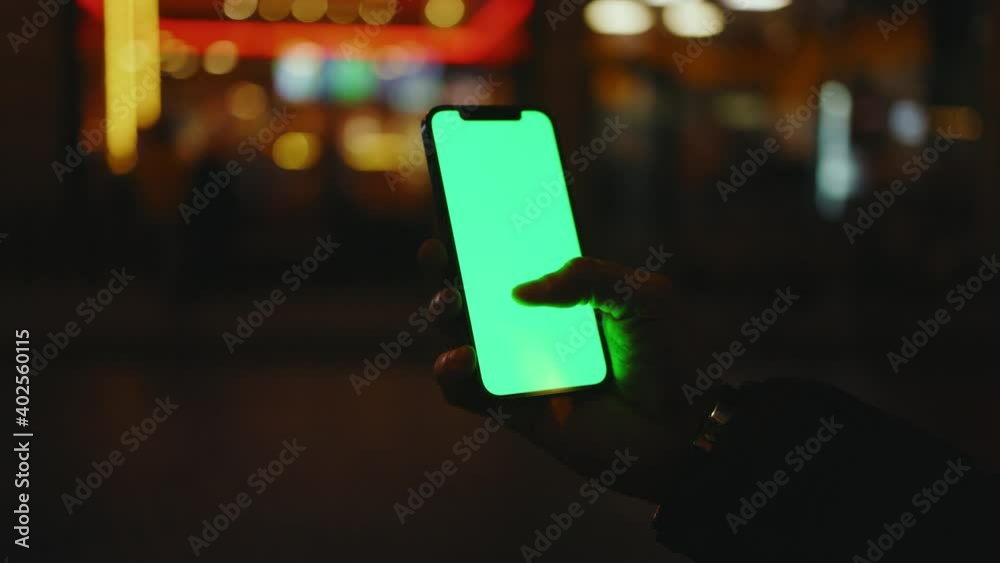 Close up hands man use phone with vertical green screen stand at night city. Evening smartphone display application. Technology touchscreen cellular. Slow motion Close up hands man use phone with vertical green screen stand at night city. Evening smartphone display application. Technology touchscreen cellular. Slow motion