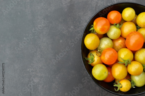 Top view and selective focus of fresh cherry tomatoes or the scientific name called as Solanum lycopersicum in the black bowl over black background.