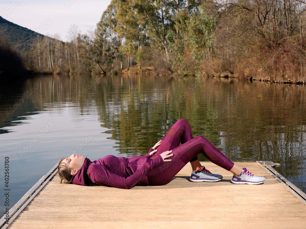Young athlete woman rests lying on the platform of a river