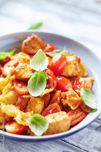 Farfalle pasta with chicken breast, cherry tomatoes and fresh basil. Bright wooden background.