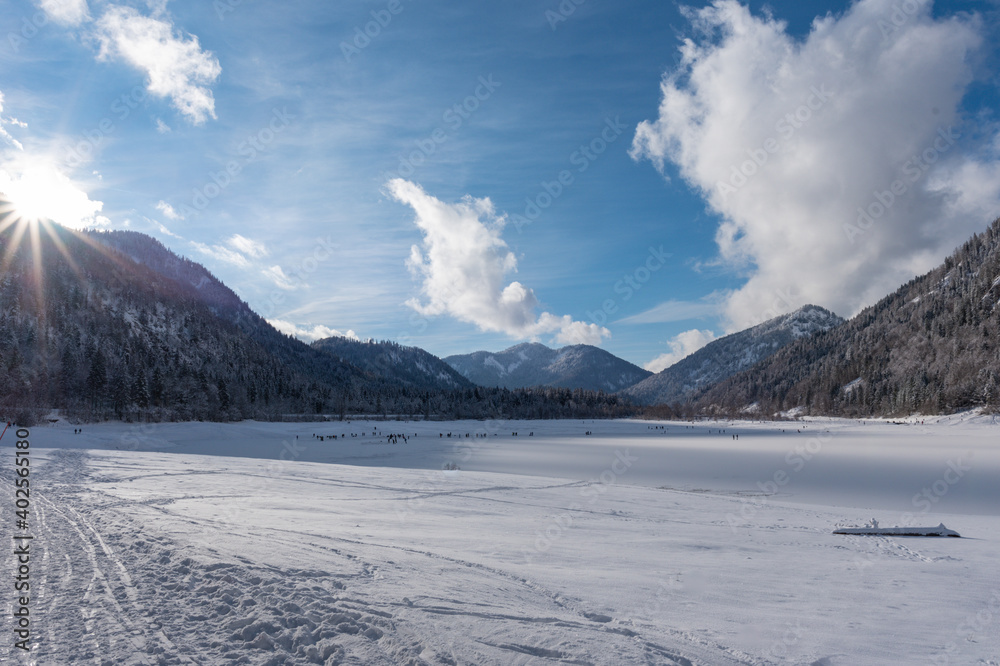 Verschneite Berge  am gefrorenen See im Chiemgau bei blauen Himmel mit Wolken