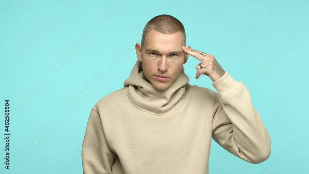 Slow motion of handsome hip-hop style man with tattoos on head and hands, pointing two fingers at temple, asking to think, use your brain, standing over blue background Slow motion of handsome hip-hop style man with tattoos on head and hands, pointing two fingers at temple, asking to think, use your brain, standing over blue background