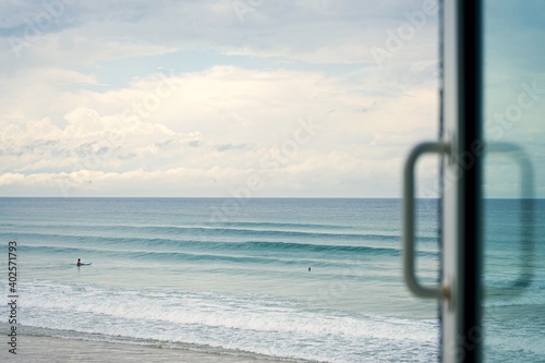 Looking out of the window of a beach house right on the water front at the beautiful blue waves rolling to shore. Perfect bedroom views of surfers photo