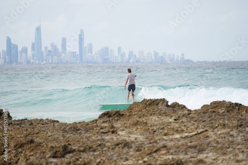 A surfer rides a longboard along a perfect tropical turquoise wave with the world famous Surfers Paradise skyline behind him