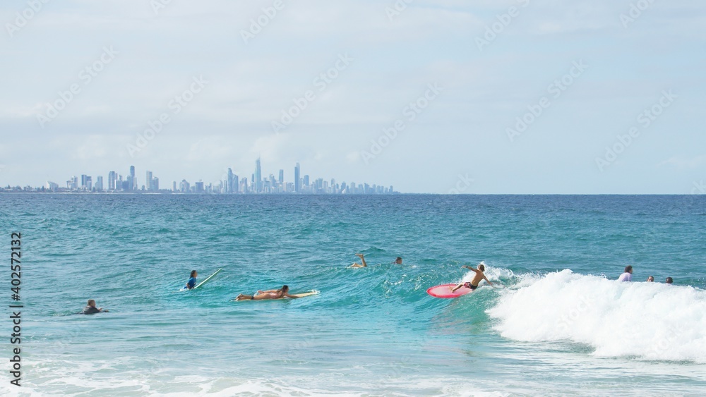 A young blonde Australian kid surfs in front of Surfers Paradise on a bright pink surfboard