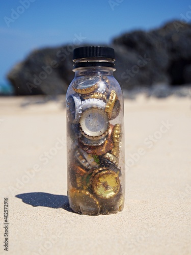 Plastic bottle filled with old, rusty, discarded berr bottle tops found in the sand photo