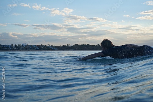 A surfer paddles for a wave with Noosa Main beach behind him
