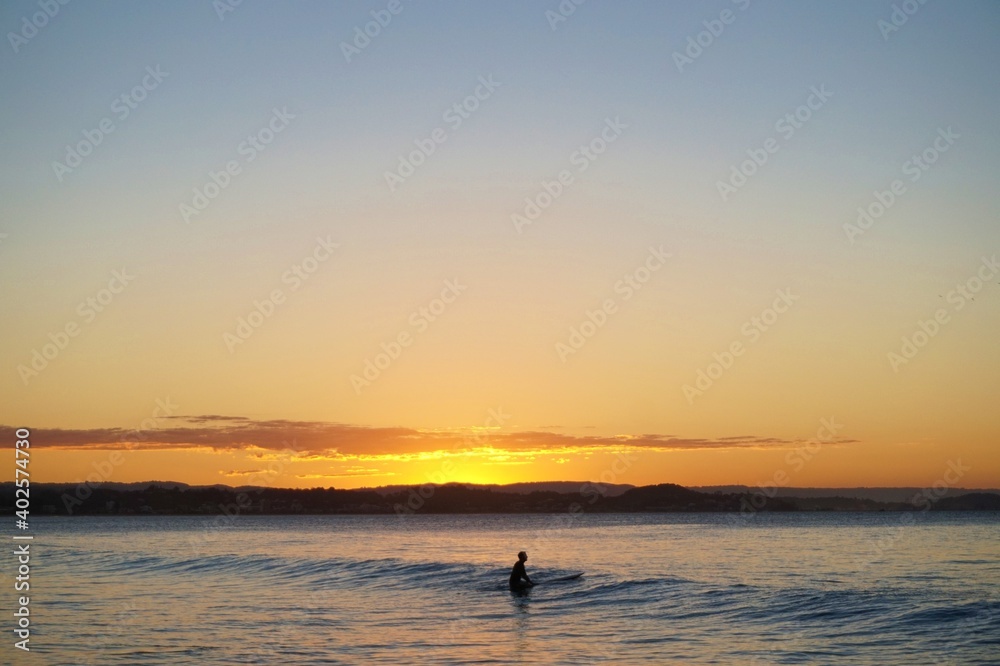 A silhouette of a surfer drifts over a small wave as the sunset bathes the sky in bright colours - Gold Coast