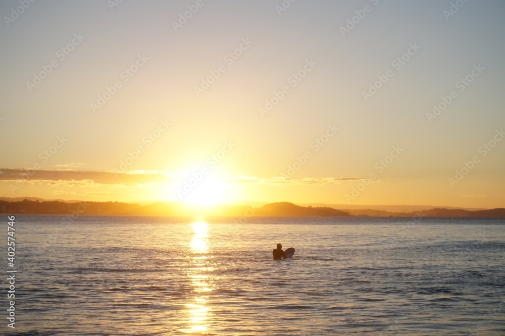 Sunlight reflects off the calm water surface as a surfer sits on his surfboard - Greenmount, Gold Coast